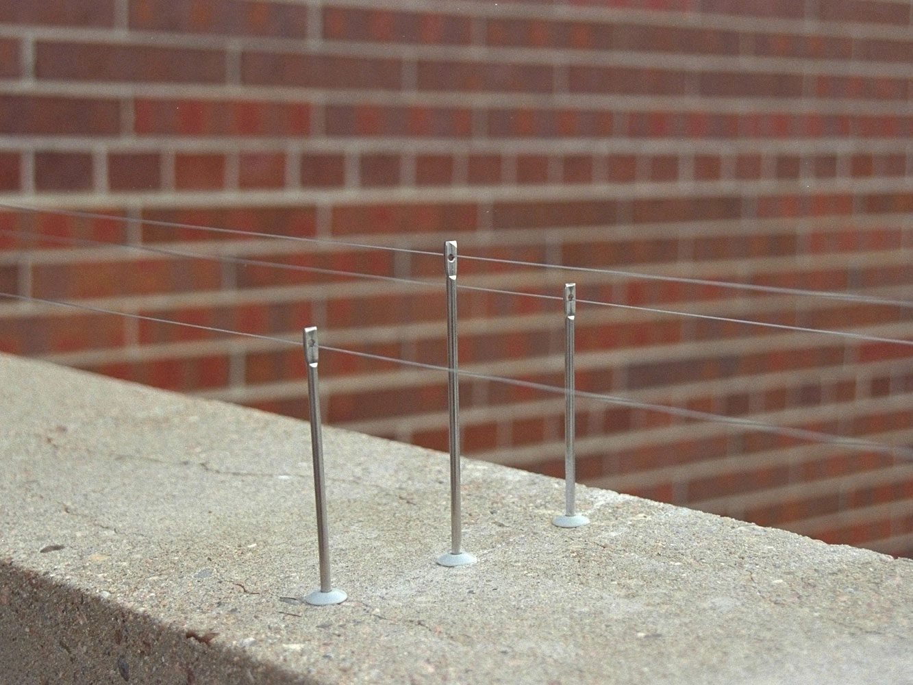 Nixalite stainless-steel post and tensioned wire deterrent installed on a commercial brick parapet